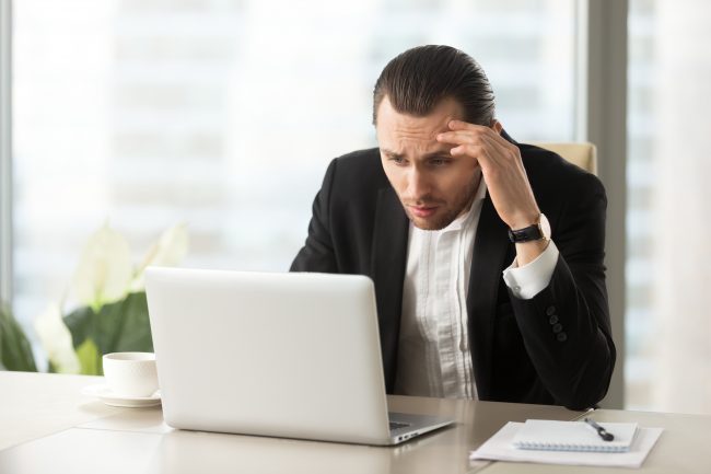 Upset confused businessman looking at laptop screen at workplace